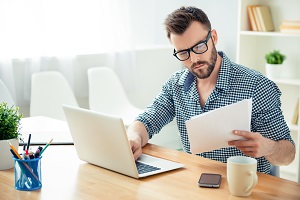 Young Man Looking Reading Document in Front Of Computer